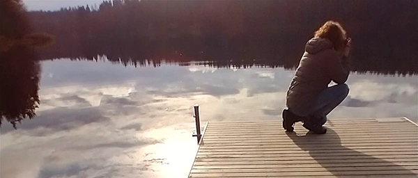nainen laiturilla kuvaamassa järveä